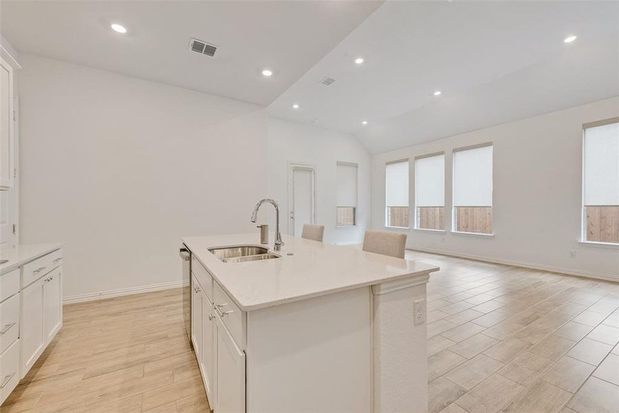 Kitchen with light wood finished floors, an island with sink, white cabinets, vaulted ceiling, and light countertops Kitchen with light wood finished floors, an island with sink, white cabinets, vaulted ceiling, and light countertops