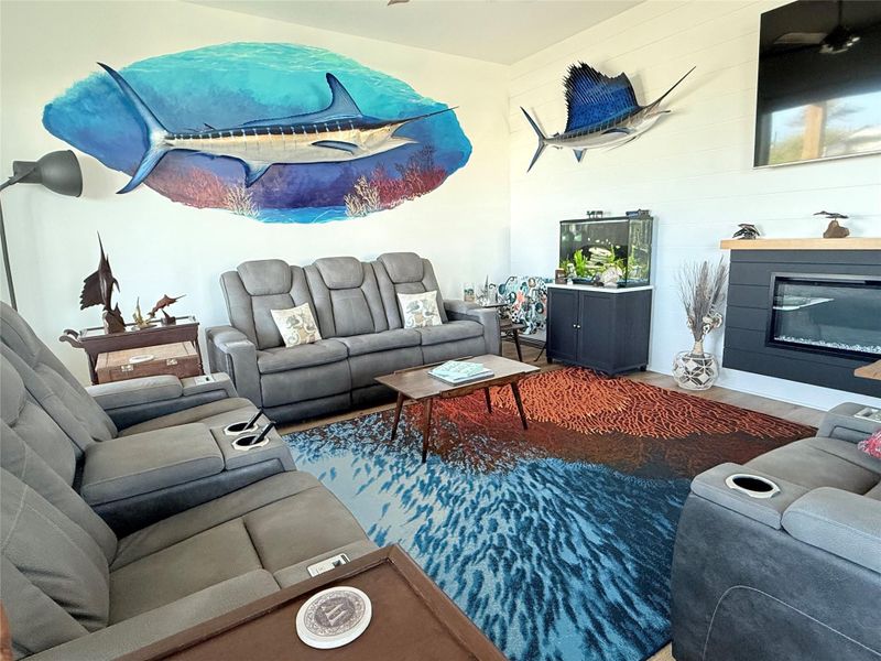 This marine inspired living space includes plush gray reclining sofas, a unique ocean-themed area rug, and decorative accents, creating a relaxed, atmosphere.