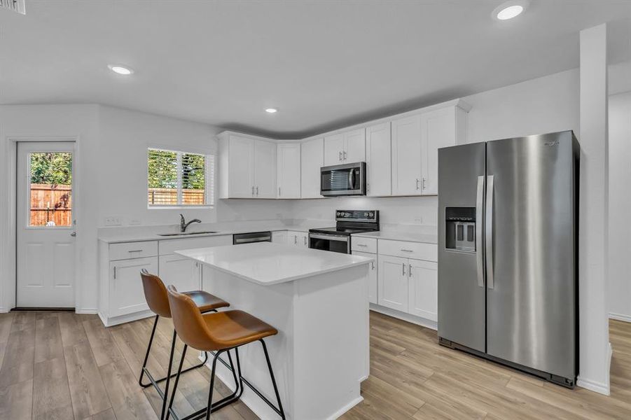 Kitchen featuring appliances with stainless steel finishes, white cabinetry, recessed lighting, a kitchen breakfast bar, and light wood finished floors