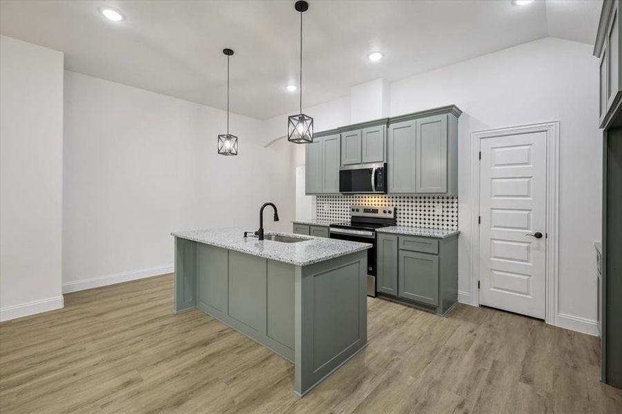 Kitchen with stainless steel appliances, tasteful backsplash, gray cabinets, a center island with sink, and pendant lighting Kitchen with stainless steel appliances, tasteful backsplash, gray cabinets, a center island with sink, and pendant lighting