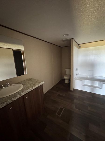 Wood-look flooring runs throughout a bathroom complete with a soaking tub and stone-look vanity.
