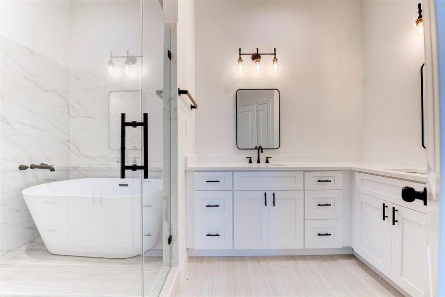 Primary bath featuring a freestanding soaking tub set within the walk-in shower, creating a true spa-like retreat. Dual sink areas with separate vanities offer added functionality, all finished with quartz countertops, shaker cabinetry, and matte black fixtures.