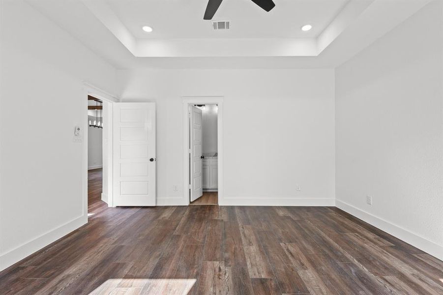 Unfurnished bedroom with a tray ceiling, ceiling fan, dark hardwood / wood-style flooring, and ensuite bathroom