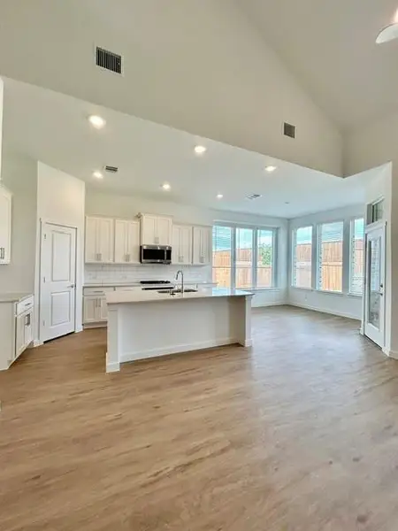 Modern kitchen and living area featuring wood-finish flooring, vaulted ceilings, and recessed lighting Modern kitchen and living area featuring wood-finish flooring, vaulted ceilings, and recessed lighting