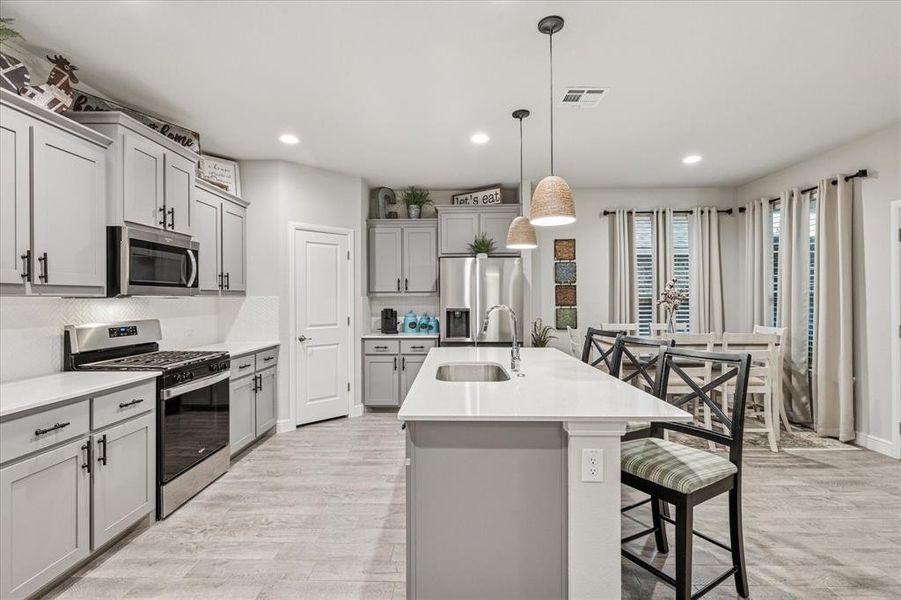 Kitchen with appliances with stainless steel finishes, a sink, gray cabinets, light wood-type flooring, and recessed lighting Kitchen with appliances with stainless steel finishes, a sink, gray cabinets, light wood-type flooring, and recessed lighting