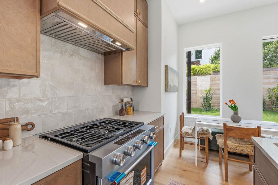 Gourmet kitchen featuring a professional-grade gas range, stainless steel vent hood, light wood-finish cabinetry, white subway tile backsplash, and light-toned countertops