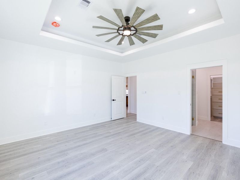 This spacious, bright room features sleek light wood flooring, a modern ceiling fan, and recessed lighting. The white walls enhance the airy feel, and there are two doorways leading to adjacent rooms, adding to the open layout.