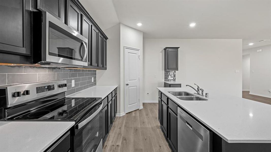 Modern kitchen featuring dark cabinetry, white countertops, stainless steel appliances, a subway tile backsplash, and wood-finish flooring