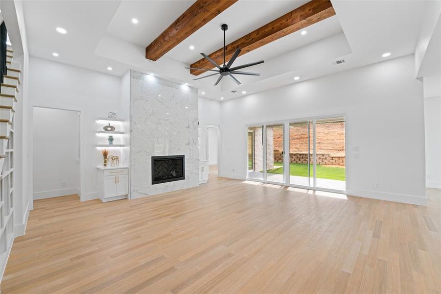 Unfurnished living room with a towering ceiling, beam ceiling, light wood-style flooring, a ceiling fan, and a fireplace