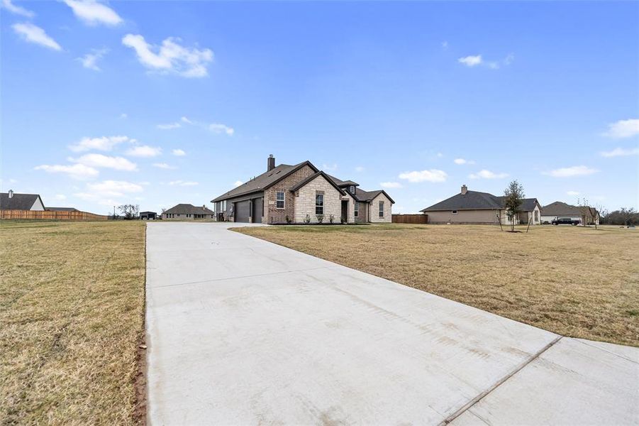 View of front facade featuring a residential view, concrete driveway, a chimney, and stone siding