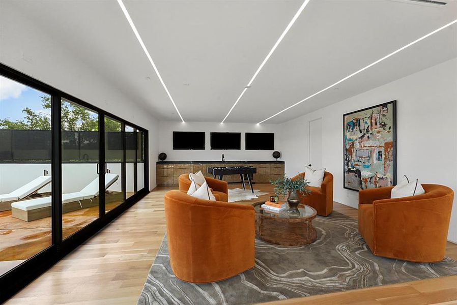 Spacious entertainment room featuring recessed linear lighting and wood-finish flooring