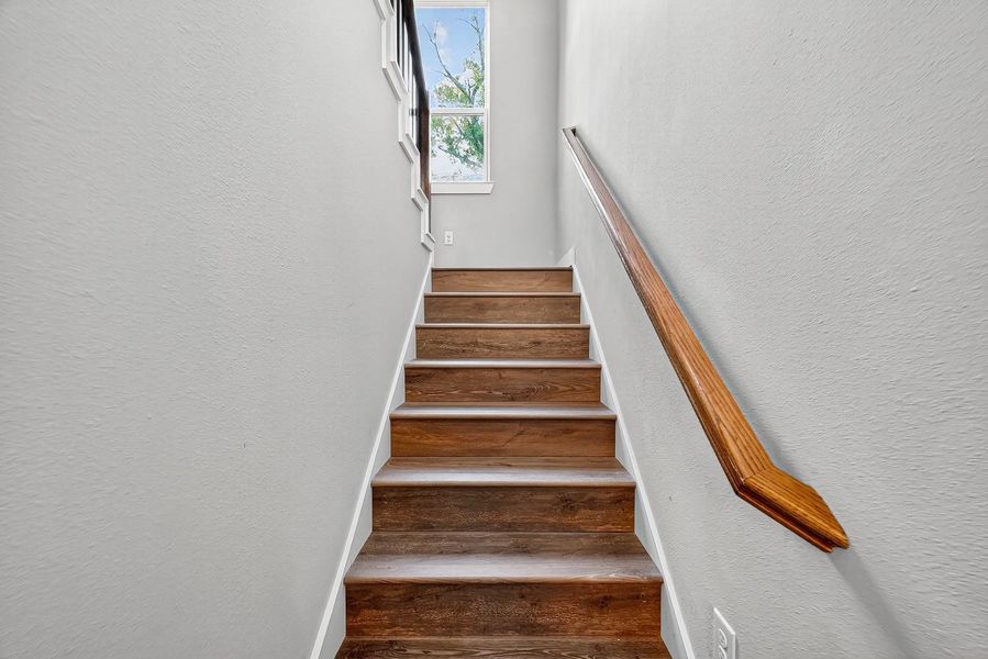 The staircase rises with quiet drama, with a window illuminating the ascent, creating a subtle interplay of shadow and light.