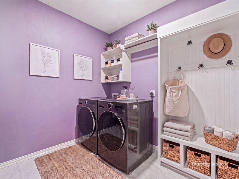 Functional laundry room with built-in upper shelving and a mudroom-style bench with cubbies and hooks for everyday organization. Tile flooring and full-size washer and dryer connections add convenience. This photo has been digitally staged to illustrate the possibilities of the home's aesthetic and potential design. Some furnishings and décor shown are for visual inspiration.