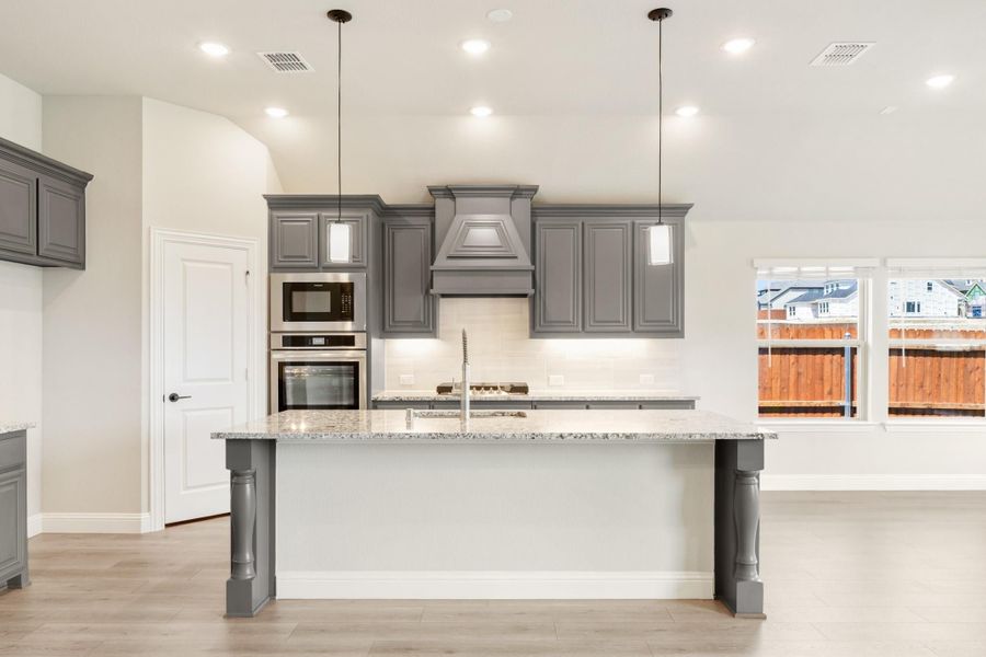 Kitchen with gray cabinets, granite island, stainless steel appliances, and decorative range hood Kitchen with gray cabinets, granite island, stainless steel appliances, and decorative range hood