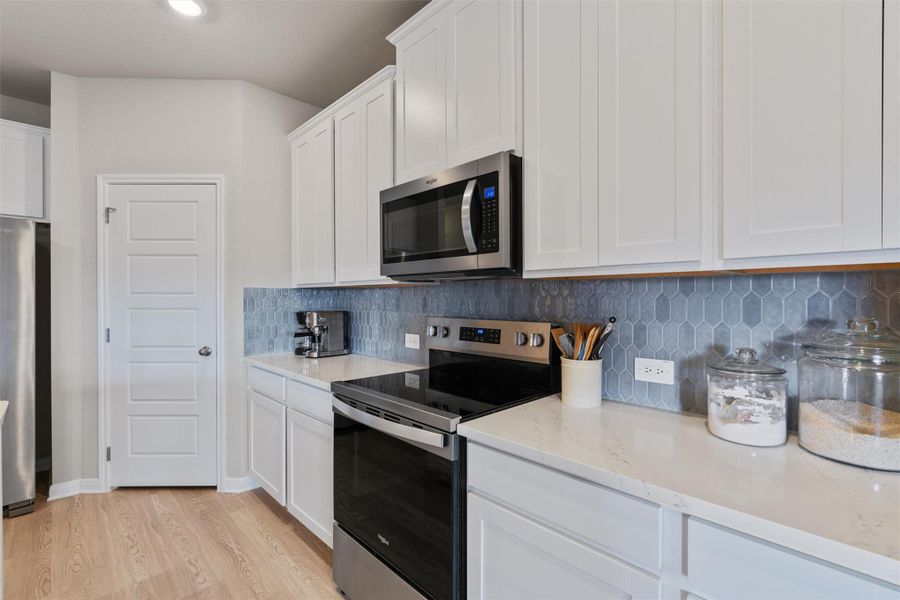 Contemporary kitchen showcasing white shaker cabinetry, stainless steel appliances, light-toned wood-finish flooring, white countertops, and a blue picket tile backsplash Contemporary kitchen showcasing white shaker cabinetry, stainless steel appliances, light-toned wood-finish flooring, white countertops, and a blue picket tile backsplash