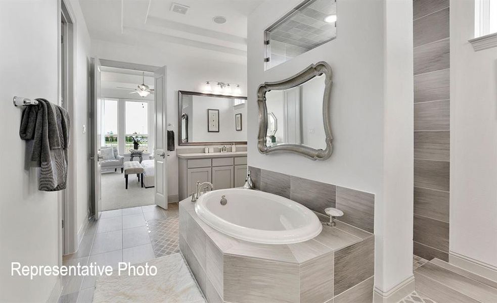 Bathroom featuring a built-in soaking tub, dual vanity with framed mirror, a separate shower enclosure, and tiled flooring