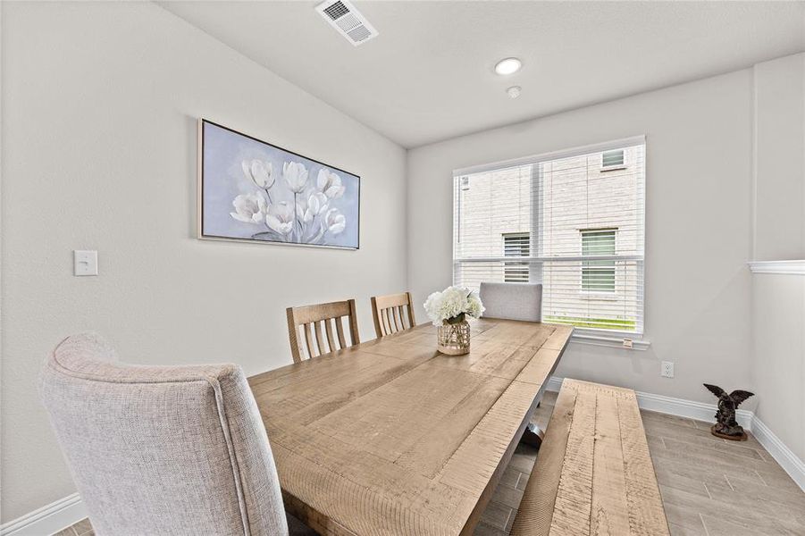 This bright and airy dining room boasts excellent natural lighting, streaming in through a large window that overlooks the property. The spacious layout comfortably accommodates a large, rustic wooden dining table and matching bench, making it perfect for family gatherings and entertaining.