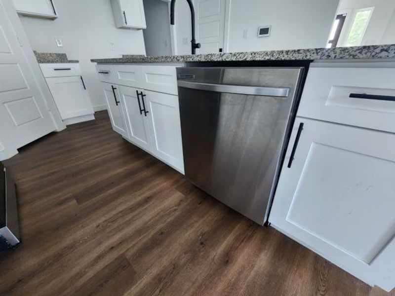 Kitchen featuring dishwasher, white cabinetry, dark wood finished floors, and dark stone counters Kitchen featuring dishwasher, white cabinetry, dark wood finished floors, and dark stone counters