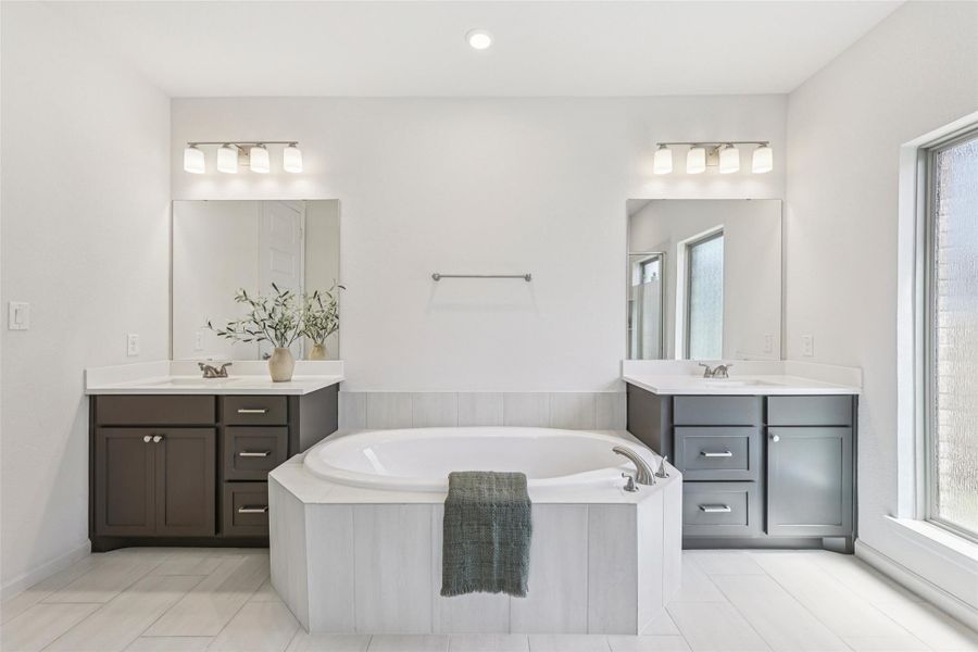 Bathroom with a built-in bathtub, dual vanities with white countertops, and light-colored tile flooring