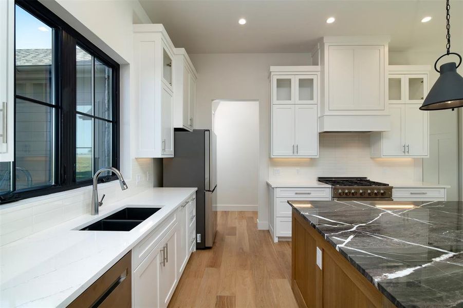 Kitchen with white cabinetry, decorative light fixtures, and dark stone counters