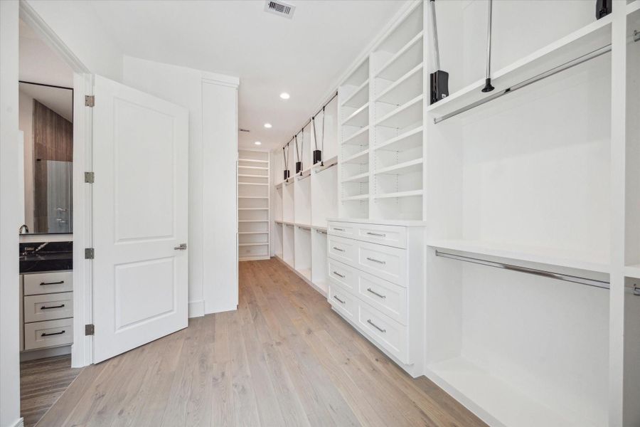 Spacious primary closet features built-in storage and ample room for hanging clothes with pull-down bars for accessing all custom storage solutions. Spacious primary closet features built-in storage and ample room for hanging clothes with pull-down bars for accessing all custom storage solutions.