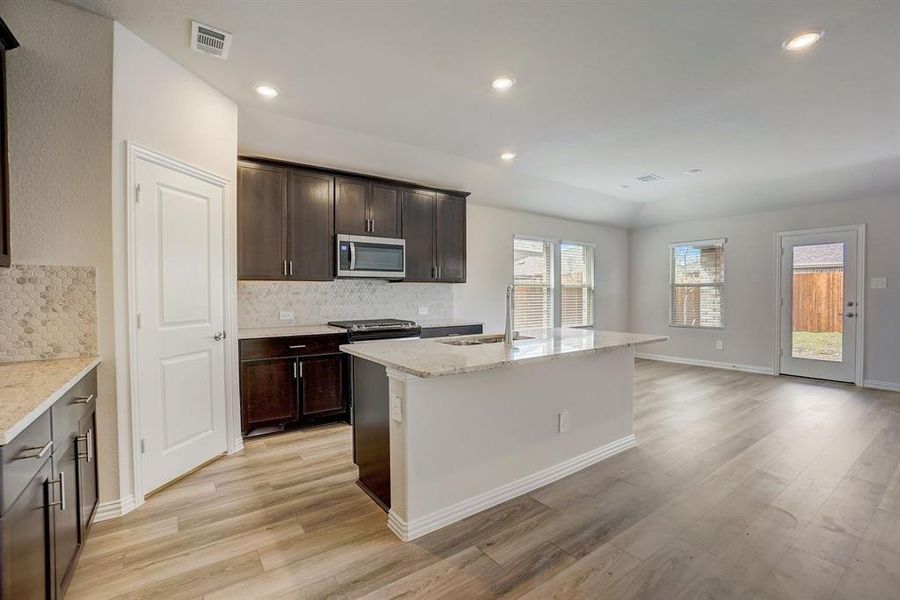 Kitchen featuring backsplash, a kitchen island with sink, light hardwood / wood-style floors, light stone countertops, and sink