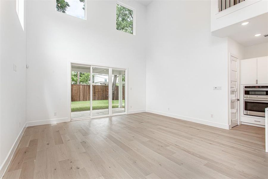 Unfurnished living room featuring a high ceiling, light wood finished floors, and baseboards