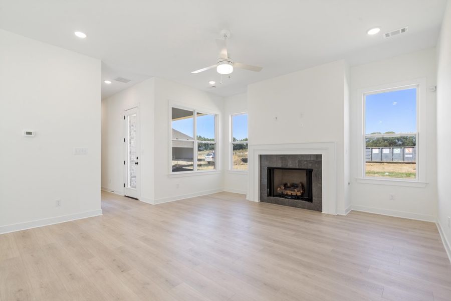 Light-filled living area featuring wood-finish flooring, a white mantel fireplace with a dark stone surround, recessed lighting, and a central ceiling fan Light-filled living area featuring wood-finish flooring, a white mantel fireplace with a dark stone surround, recessed lighting, and a central ceiling fan