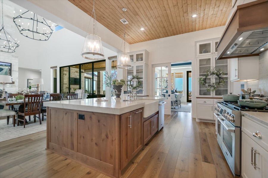 Kitchen featuring appliances with stainless steel finishes, custom exhaust hood, a chandelier, a sink, and light countertops Kitchen featuring appliances with stainless steel finishes, custom exhaust hood, a chandelier, a sink, and light countertops