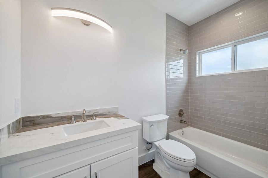 This stylish full bathroom combines modern simplicity with timeless finishes. A white shaker-style vanity is topped with an elegant stone-look counter and backsplash, complemented by brushed-metal fixtures. The tub and shower surround features glossy subway tile extending to the ceiling, creating a clean and sophisticated appearance. A wide window introduces natural light, while the streamlined lighting fixture and neutral palette complete the bright, contemporary design. This stylish full bathroom combines modern simplicity with timeless finishes. A white shaker-style vanity is topped with an elegant stone-look counter and backsplash, complemented by brushed-metal fixtures. The tub and shower surround features glossy subway tile extending to the ceiling, creating a clean and sophisticated appearance. A wide window introduces natural light, while the streamlined lighting fixture and neutral palette complete the bright, contemporary design.