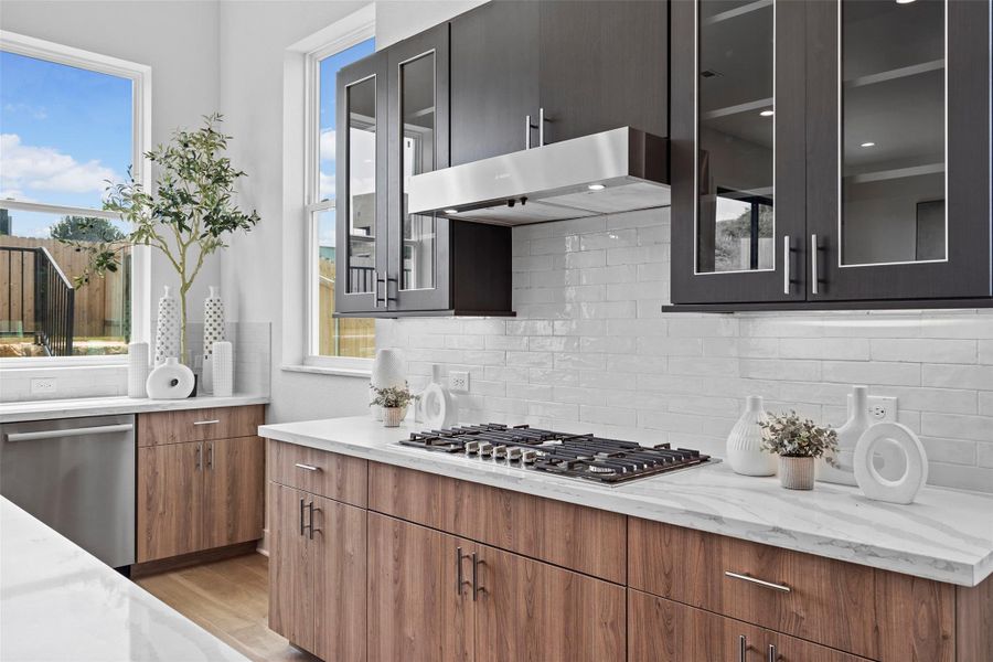 Kitchen with glass insert cabinets, stainless steel appliances, light stone counters, and decorative backsplash