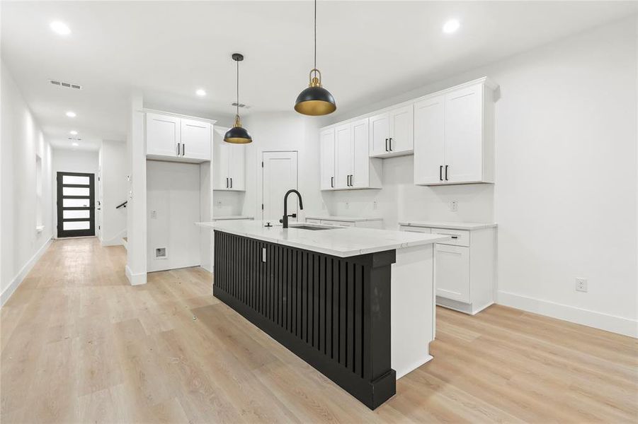 Kitchen with white cabinets, an island with sink, recessed lighting, light wood-type flooring, and decorative light fixtures Kitchen with white cabinets, an island with sink, recessed lighting, light wood-type flooring, and decorative light fixtures