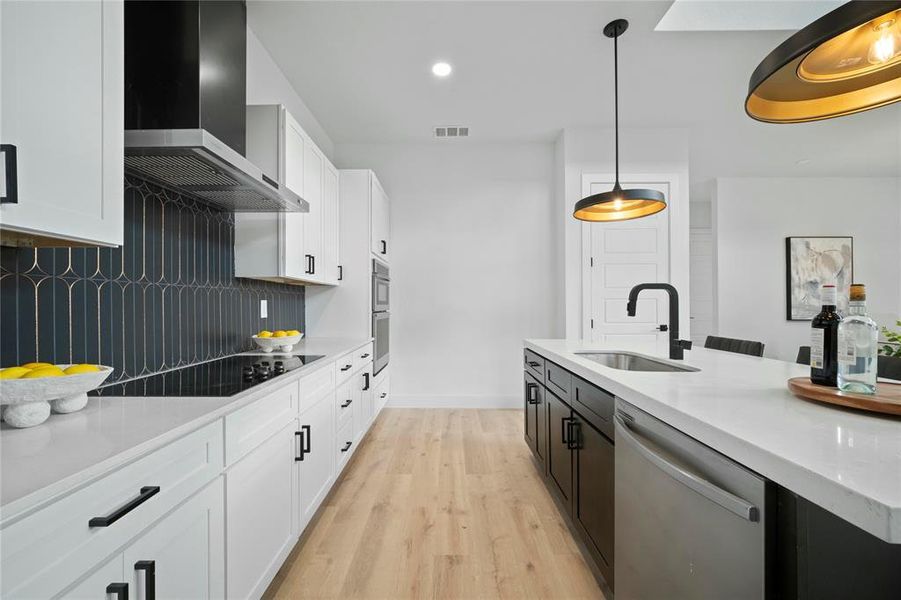 Kitchen featuring dishwasher, wall chimney range hood, backsplash, hanging light fixtures, and white cabinetry Kitchen featuring dishwasher, wall chimney range hood, backsplash, hanging light fixtures, and white cabinetry