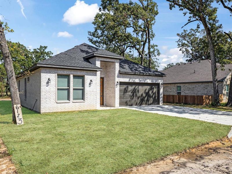 View of front facade featuring roof with shingles, concrete driveway, brick siding, and a garage
