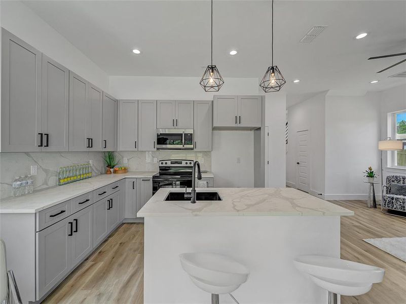 Kitchen with backsplash, stainless steel appliances, light stone counters, an island with sink, and light wood-type flooring