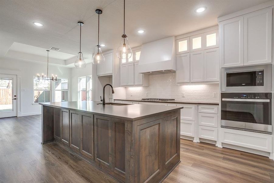 Kitchen featuring stainless steel appliances, white cabinetry, premium range hood, decorative light fixtures, and recessed lighting