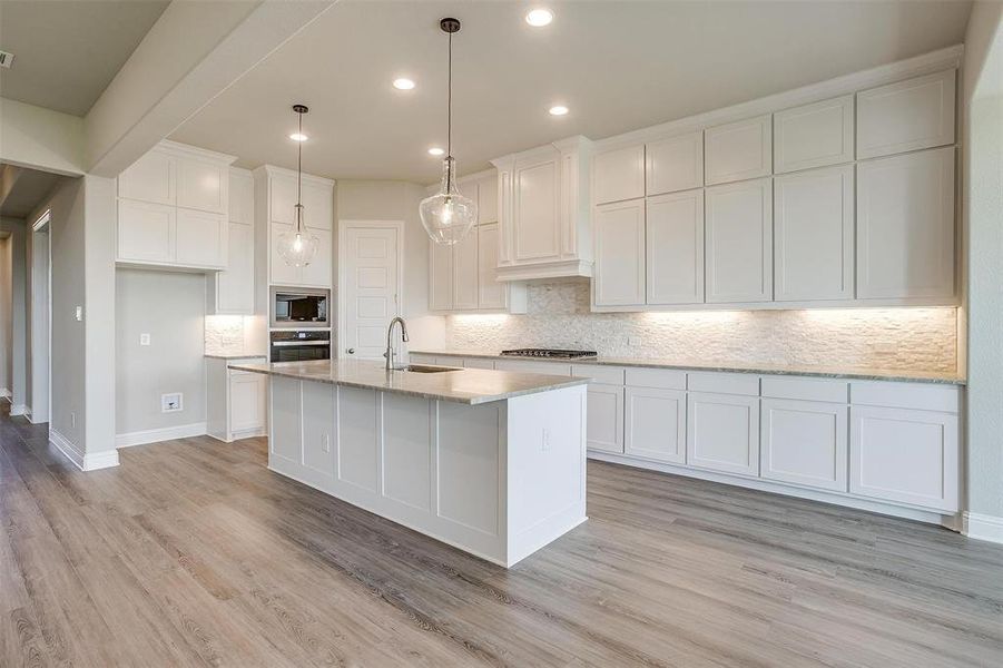 Kitchen featuring light wood-type flooring, stainless steel appliances, a kitchen island with sink, sink, and white cabinetry