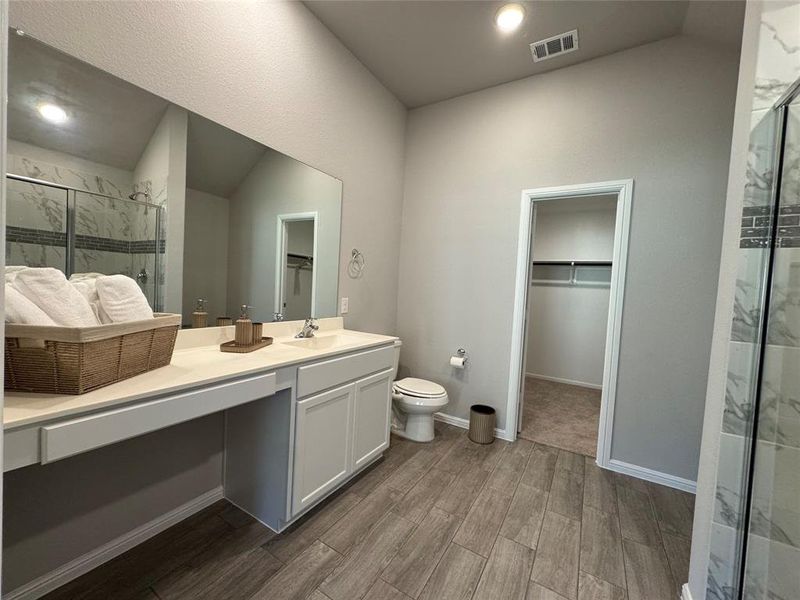 Bathroom featuring a double vanity with ample counter space, a separate toilet area, and wood-finish flooring Bathroom featuring a double vanity with ample counter space, a separate toilet area, and wood-finish flooring