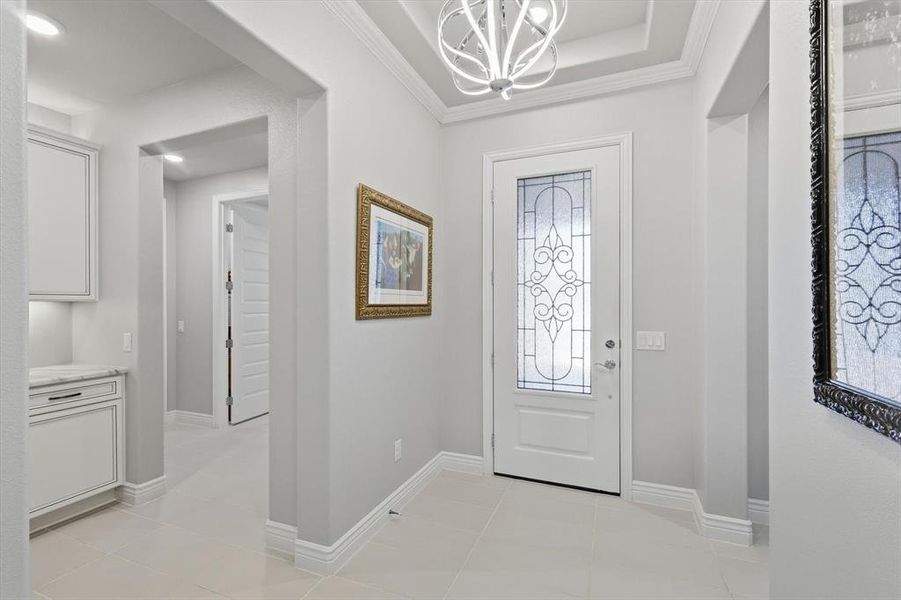 Elegant entry featuring a decorative glass front door, tray ceiling with a contemporary chandelier, and large format tile flooring