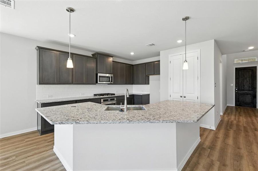 Kitchen featuring appliances with stainless steel finishes, wood finished floors, decorative backsplash, dark brown cabinets, and light stone counters Kitchen featuring appliances with stainless steel finishes, wood finished floors, decorative backsplash, dark brown cabinets, and light stone counters