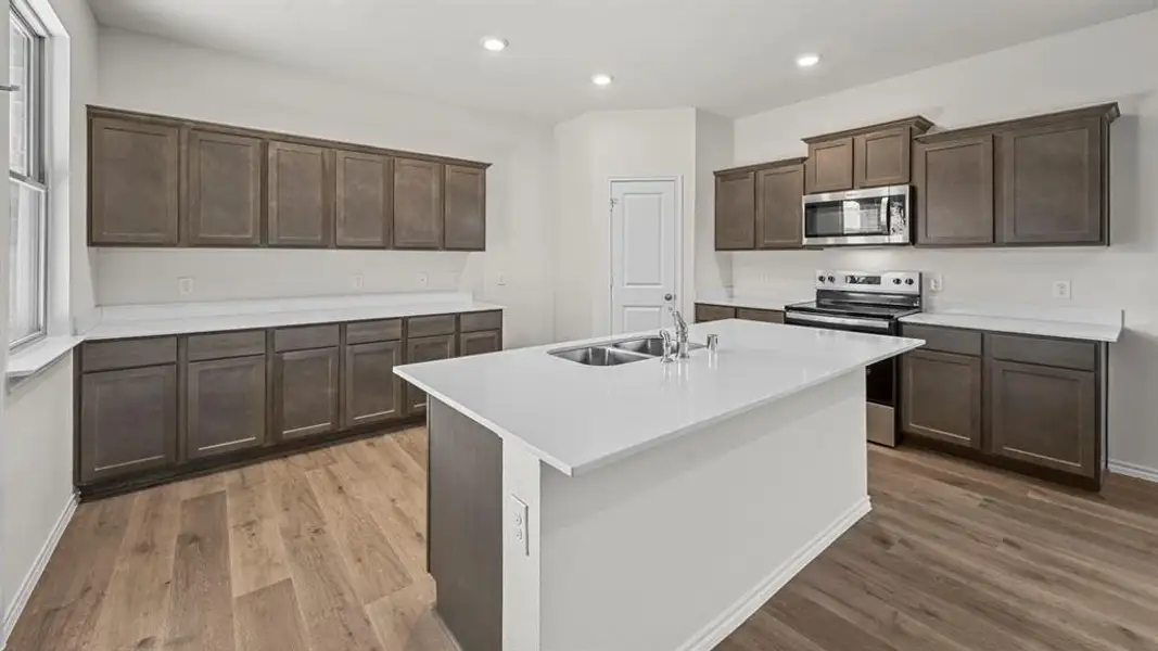 Kitchen featuring a central island with a double basin sink, stainless steel appliances, extensive cabinetry, light countertops, and wood-finish flooring