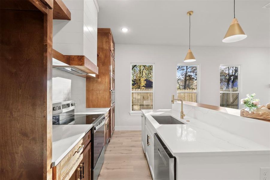 Kitchen with sink, hanging light fixtures, light hardwood / wood-style flooring, an island with sink, and appliances with stainless steel finishes