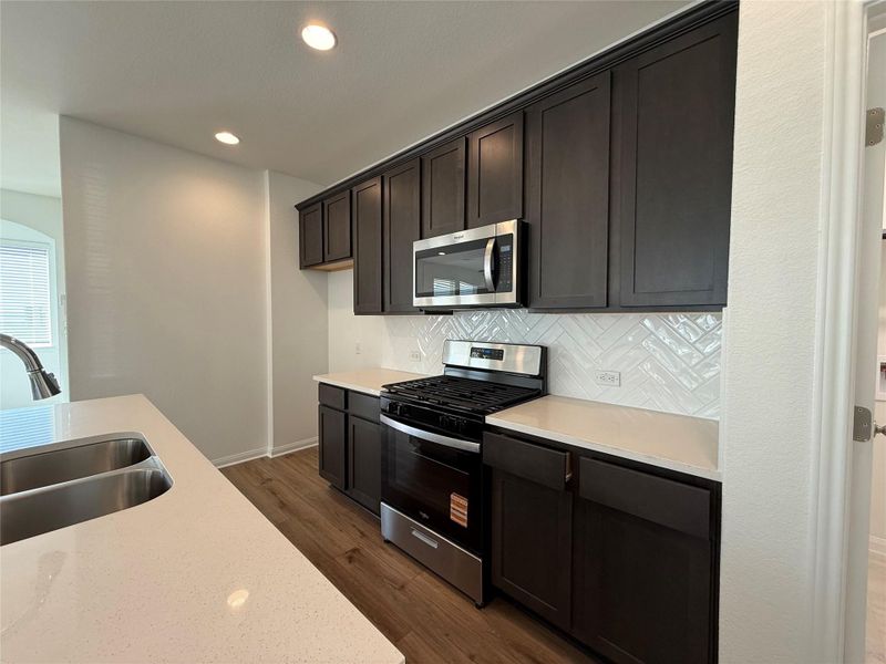 Kitchen with stainless steel appliances, decorative backsplash, dark wood finished floors, recessed lighting, and light stone countertops Kitchen with stainless steel appliances, decorative backsplash, dark wood finished floors, recessed lighting, and light stone countertops