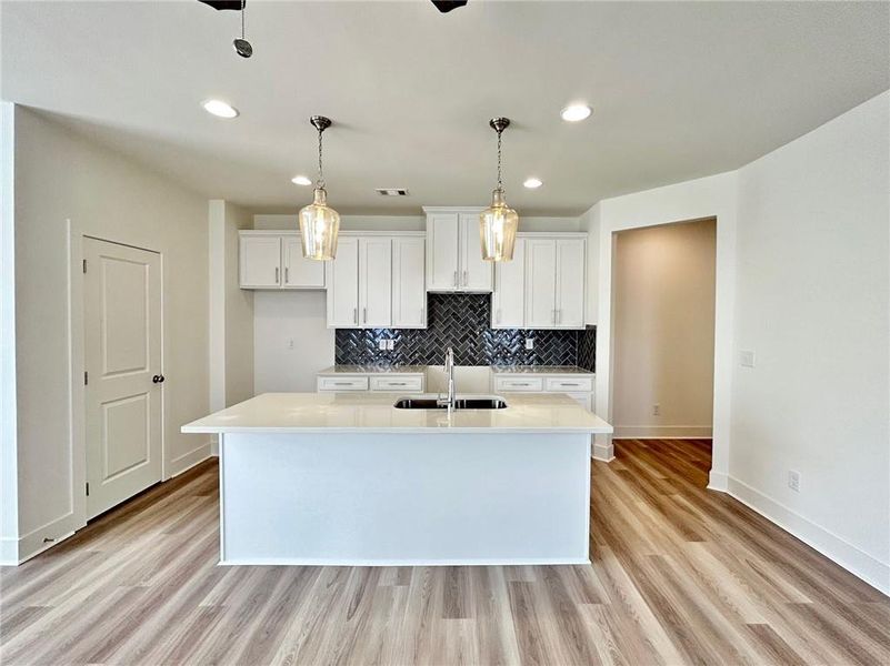 Kitchen featuring pendant lighting, white cabinets, an island with sink, and light hardwood / wood-style flooring