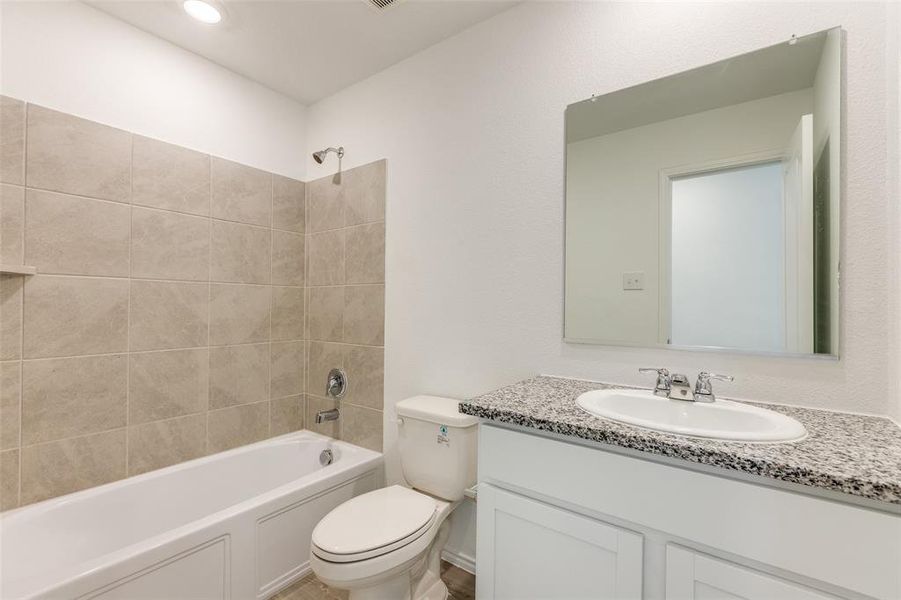 Full bathroom with tiled shower / bath combo, toilet, and vanity