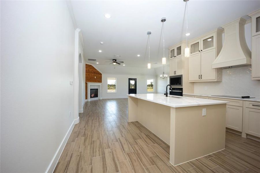 Kitchen featuring custom exhaust hood, wood tiled floors, open floor plan, a brick fireplace, and a ceiling fan