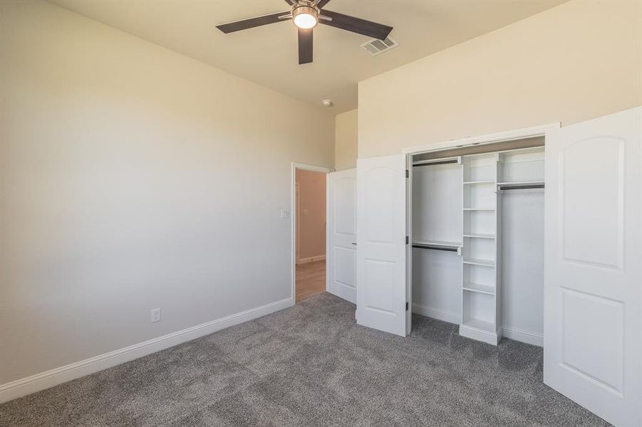 Unfurnished bedroom featuring dark colored carpet, ceiling fan, lofted ceiling, and a closet