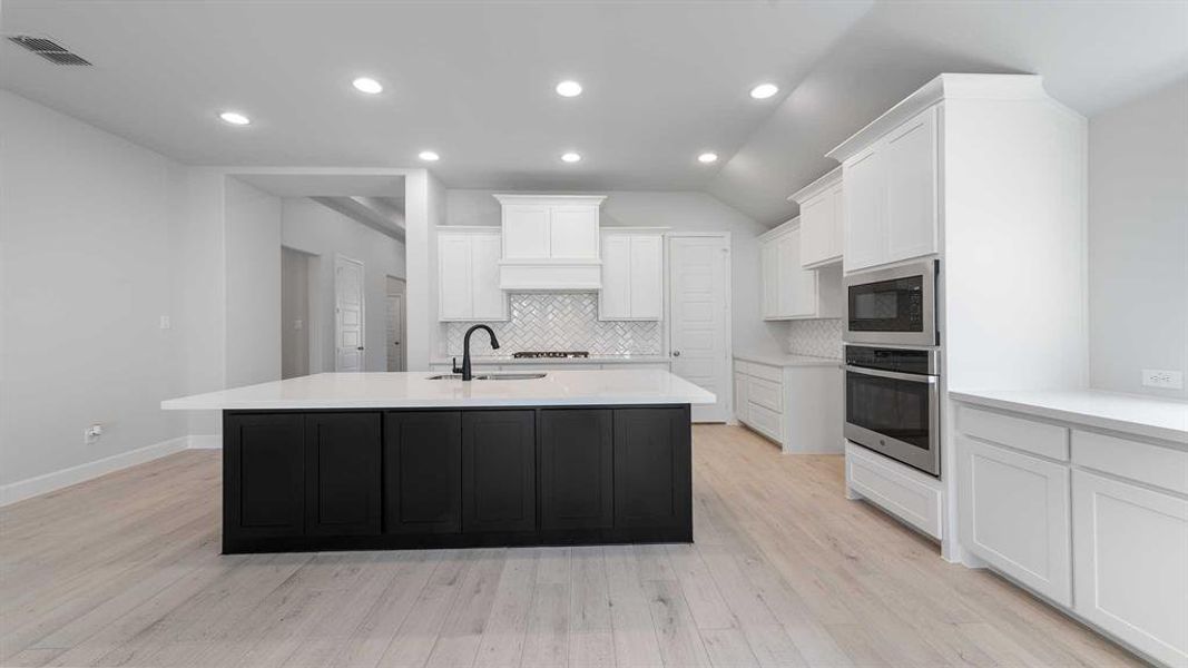 Kitchen with light hardwood / wood-style floors, decorative backsplash, stainless steel oven, white cabinetry, and built in microwave