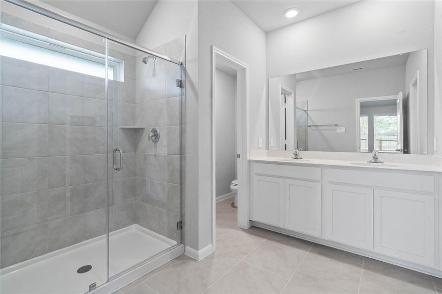 A bright and functional primary bath offering dual sinks for busy mornings, a large mirror, and a modern glass-enclosed shower, creating a serene and efficient space.