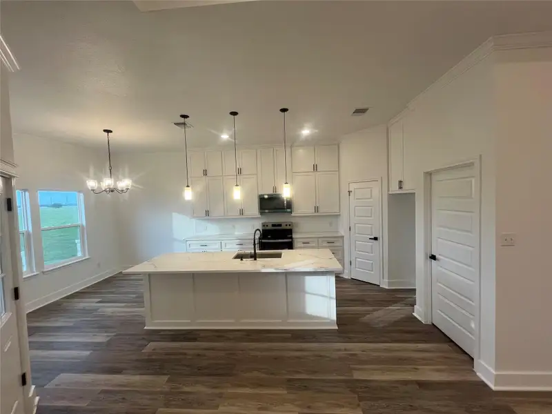 This photo showcases a modern kitchen with a large island, pendant lighting, and medium gray/wood water proof plank flooring. It features white cabinetry, stainless steel appliances, and ample natural light from large windows.
